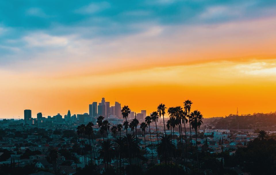 Los Angeles skyline and palm trees beneath an orange and blue sky